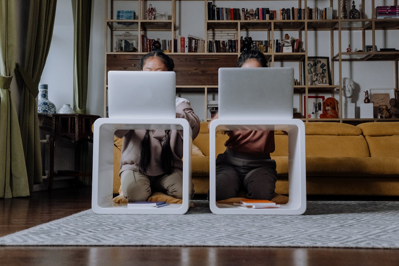 Two children kneeling with laptops at modern tables in an inviting living room.