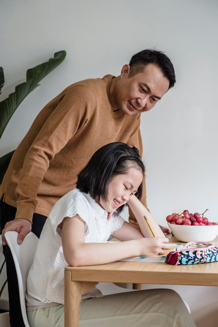 A father helps his daughter with homework at a dining table, fostering family bonding and education.